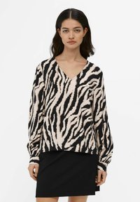 Langærmet top med V-udskæring, der har et beige og sort zebra-stribet mønster. Lavet af et blødt stof og parret med en sort nederdel.