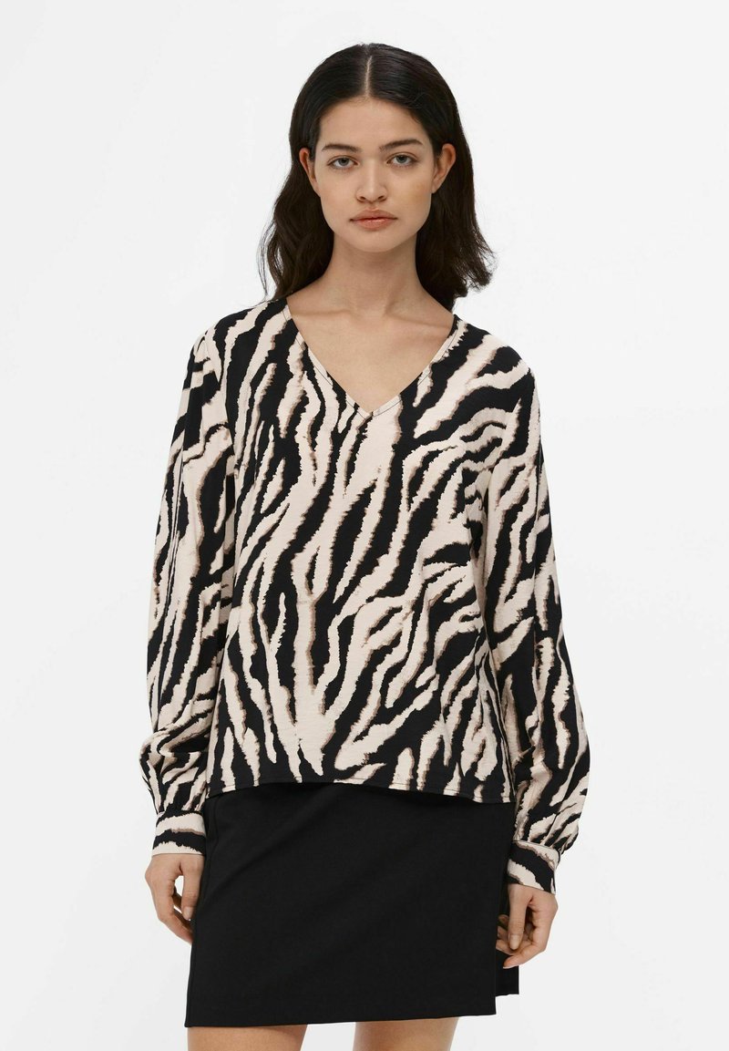 Langærmet top med V-udskæring, der har et beige og sort zebra-stribet mønster. Lavet af et blødt stof og parret med en sort nederdel.