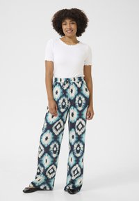 Laiad püksid, millel on sinine, must ja kreemjas ikat muster, valmistatud pehmest kangast ning elastse vöökoha ja nööriga.