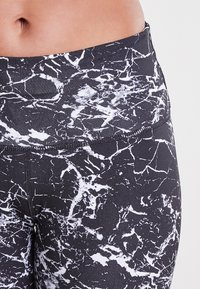 Leggings taille haute dans un motif marbré noir et blanc, fabriqués en tissu extensible avec une finition lisse et texturée et des coutures renforcées.