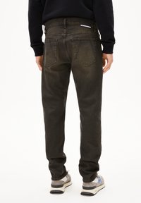 Jeans verde oliva oscuro con corte recto, diseño de cinco bolsillos y una cinturilla con marca. Textura notablemente descolorida y detalles de costura.