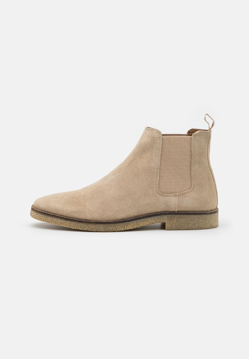 Bottes chevillières en suede beige avec des panneaux latéraux élastiques, une languette et une semelle texturée avec un léger talon. Conception à bout rond.