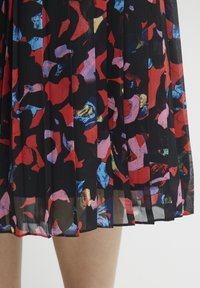 Zwarte geplooide rok met een levendig abstract patroon in rode, roze, blauwe en gouden tinten, gemaakt van lichte, doorschijnende stof.