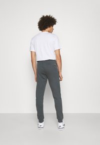 Grijze sweatpants voor heren gemaakt van zachte stof, met een taps toelopend ontwerp, elastische tailleband en een enkele achterzak. Draagt een witte T-shirt.