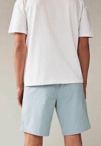 Tricou alb cu mânecă scurtă asortat cu pantaloni scurți de culoare albastră deschisă. Pantalonii scurți au o textură netedă și o croială dreaptă, terminându-se deasupra genunchiului.