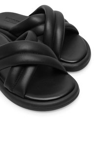 Zwarte leren sandalen met een crisscross strap ontwerp, een gladde textuur en afgeronde randen, rustend op een platte zool.
