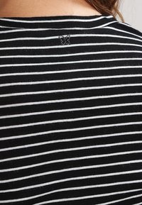 Camicia in tessuto a righe bianche e nere, in cotone leggero, con scollatura arrotondata e un piccolo logo decorativo vicino alla scollatura posteriore.