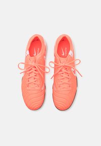 Ghete de fotbal Nike Tiempo de culoare coral deschis, cu un superior texturat, închidere cu șireturi și talpă din cauciuc negru cu detalii vizibile ale pattern-ului.