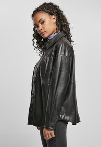 Veste en cuir noir avec col, fermeture à boutons sur le devant et deux poches poitrine. Texture lisse et coupe décontractée. Manches longues avec poignets à pression.