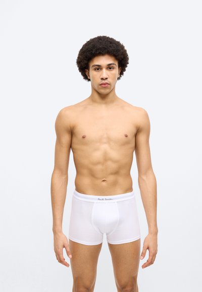 Boxer en coton blanc avec une ceinture douce portant le nom de la marque. Le modèle adopte une pose neutre, mettant en valeur la coupe et le style du vêtement.