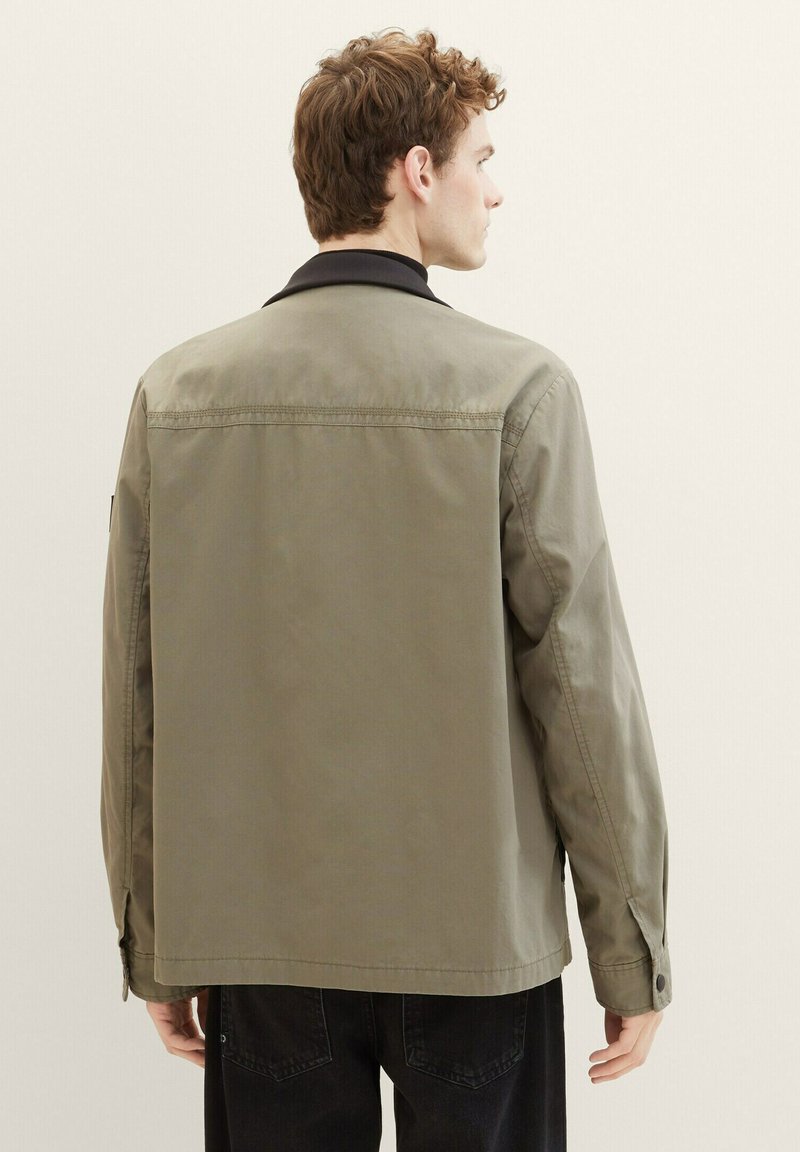 Chaqueta verde oliva con cuello negro, mangas largas y detalles de botones, con un corte recto y textura mate suave.