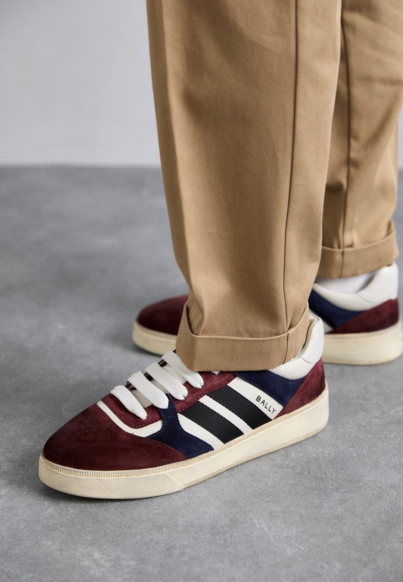 Baskets avec un mélange de bordeaux, de bleu marine et de daim blanc. Lacets blancs, trois bandes noires sur le côté, et une semelle en caoutchouc crème.