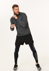 Idrætsoutfit består af en tætsiddende, mørkegrå langærmet top, sorte shorts og marineblå leggings med mønstrede detaljer; parret med sorte sneakers.
