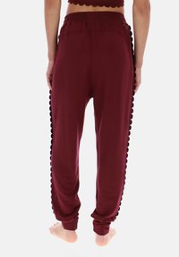 Pantaloni jogger color granata con vita elastica e dettagli neri sfrangiati lungo le cuciture laterali. Tessuto morbido, vestibilità comoda, polsini alla caviglia.