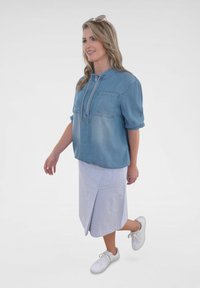 Hellblaues Denim-Blusenshirt mit kurzen Ärmeln und einer Kordelzug-Nackenpartie. Kombiniert mit einem gestreiften Midi-Rock und weißen Sneakers.