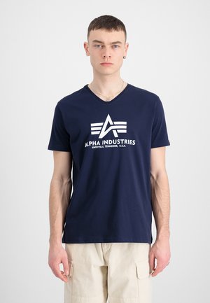 Camiseta de cuello en v de color marino hecha de algodón, con una textura suave, que presenta un diseño de logo blanco que incluye las palabras "ALPHA INDUSTRIES."