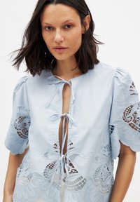 Lichtblauw blouse met een strikdetail bij de hals, met complexe bloemenborduursels en kantinzetten op korte pofmouwen.