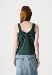 Top fără mâneci de culoare verde închis, cu bretele volănașe, design fluid și textură de țesătură netedă. Se combină cu o fustă din denim de culoare albastru deschis.