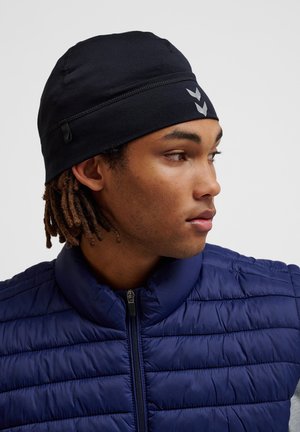 Schwarze Polyester-Mütze mit glatter Textur, ausgestattet mit einem Nahtdesign und reflektierenden Akzenten, getragen mit einer marineblauen, gesteppten Zip-Jacke.