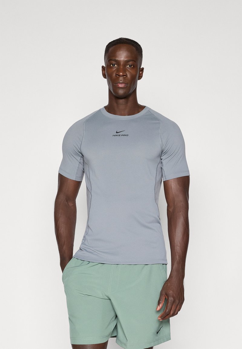 Camiseta deportiva corta de manga gris con cuello redondo y logo en el pecho, que presenta un diseño ajustado y una tela lisa y elástica.