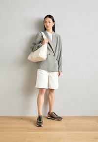 Grijs-wit geblokte blazer, witte shirt, witte korte broeken, bruin-zwarte sneakers met paarse accenten, en een roomkleurige schoudertas.