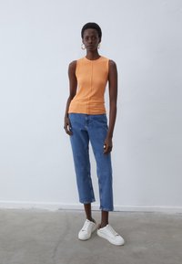 Ribbed orange sleeveless top paired with blue straight-leg denim jeans and white sneakers. Simple design with gold hoop earrings.
