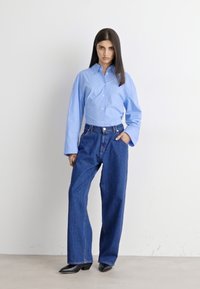 Blåstripet skjorte med knapper og lange ermer, sammen med høyt liv løse blå jeans og svarte spisse hæler.