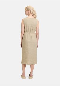 Beige linnen jurk met een getailleerde taille, mouwloos ontwerp en een zoom tot op de knie. Gladde textuur met een natuurlijke uitstraling, gecombineerd met casual schoenen.