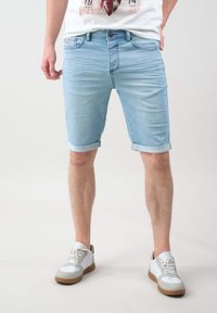 Shorts de mezclilla azul claro con puños doblados, con un ajuste estándar y un sutil desgastado, combinados con zapatillas blancas y acentos grises.