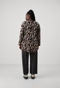 Haut à manches longues avec un motif abstrait noir et beige. Associé à un pantalon à rayures grises et des chaussures à plateforme avec des semelles épaisses.