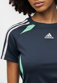 Námořnicky modré sportovní tričko se zelenými akcenty, s šedými pruhy na rukávech a malým bílým logem Adidas na hrudi.