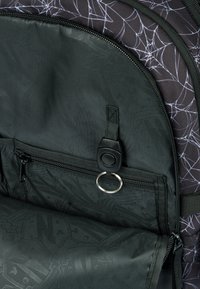 Interno di uno zaino nero con un motivo a ragnatela, fodera testurizzata, tasca con zip e un tirante rotondo con anello metallico.