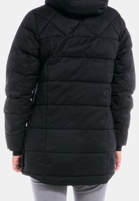 Svart puffjacka med quiltat mönster, huva och långa ärmar. Har horisontella sömmar och en något längre bakdel. Mjuk textur.