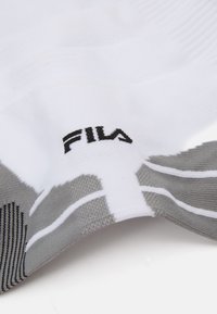 Calza sportiva bianca con un motivo testurizzato grigio, con il logo FILA nero ben visibile di lato.