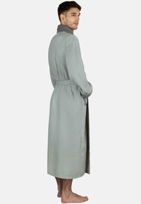 Langer, grauer, strukturierten Morgenmantel mit einem Schalkragen, tailliert mit einem Gürtel, und einem dezenten Muster. Der Stoff wirkt leicht und weich.