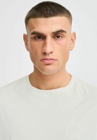 Light green cotton t-shirt with a round neck, featuring a subtle circular design on the left side. Smooth texture and fitted cut.