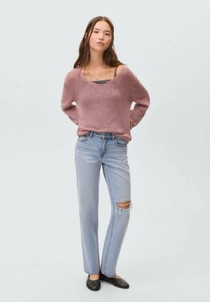 Roze gebreide trui met een ronde halslijn, gecombineerd met lichtblauwe rechte jeans met versleten kniezakken. Zwarte platte schoenen.