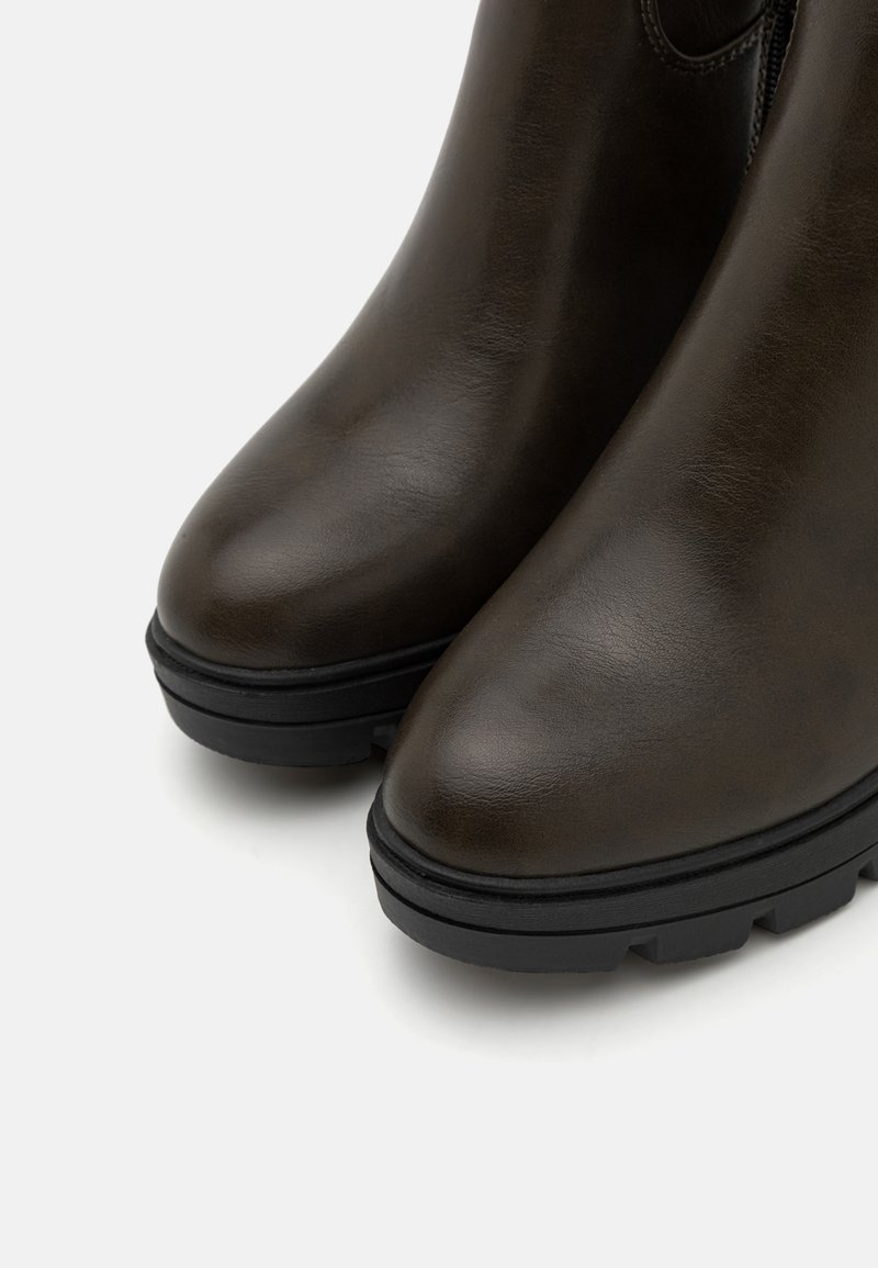 Bottines en cuir marron avec une finition brillante, à bout arrondi et semelles en caoutchouc noir robuste avec des détails de crans. Fermeture éclair sur le côté visible.