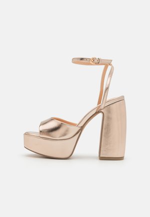Metallic rose gold platform sandals with a wide block heel and ankle strap. Smooth finish, open toe, and cushioned footbed design.