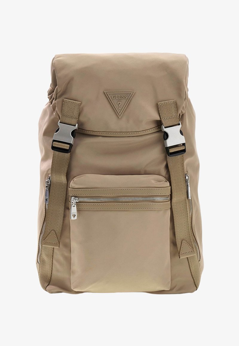 Sac à dos beige avec poche avant zippée, bretelles réglables avec boucles argentées, et patch logo triangulaire Guess sur le rabat supérieur.
