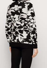 Svart och krämfärgad blommig stickad tröja med en texturerad mönster, rund halsringning och ribbade ärmslut och fåll.