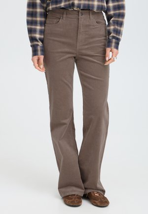 Pantalon marron à jambes droites porté avec une chemise à carreaux et des chaussures en daim marron, montrant de la taille aux pieds d'une personne debout.