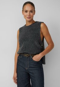Top grigio senza maniche in maglia con aperture laterali, caratterizzato da una texture morbida e una leggera elasticità, abbinato a jeans scuri a vita alta.