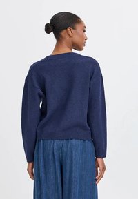 Maglione lavorato a maglia blu scuro con una vestibilità rilassata, collo e polsini a coste, e una texture morbida, abbinato a pantaloni di denim larghi.