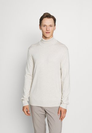 Suéter de cuello alto color beige claro en suave tejido de punto, con mangas largas y un ajuste relajado, combinado con pantalones gris claro.