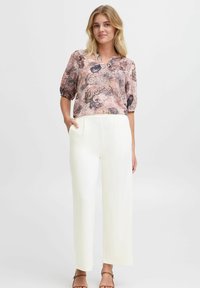 Blouse florale courte avec des manches bouffantes en motifs rose, blanc et marine, associée à un pantalon large blanc avec des poches latérales.