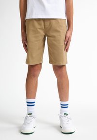 Pantaloni corti khaki realizzati in tessuto misto cotone, caratterizzati da un taglio classico, tasche laterali e orlo pulito. Indossati con sneakers bianche e calzini a righe.