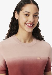 Suéter de manga corta en tonos rosa degradados, con cuello redondo acanalado, textura suave y un pequeño logo bordado en el pecho.