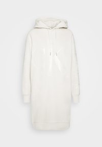 Vit hoodie klänning gjord av mjukt tyg. Har en stor, glansig "CK"-logotyp på framsidan och manschetterna med subtila detaljer. Långa ärmar.