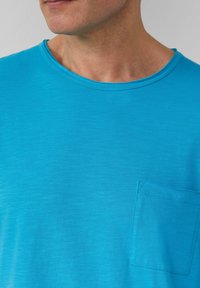 Kurzärmliges T-Shirt mit Rundhalsausschnitt in lebendigem Türkis. Verfügt über eine kleine Tasche auf der linken Brust und hat eine weiche, leichte Textur.